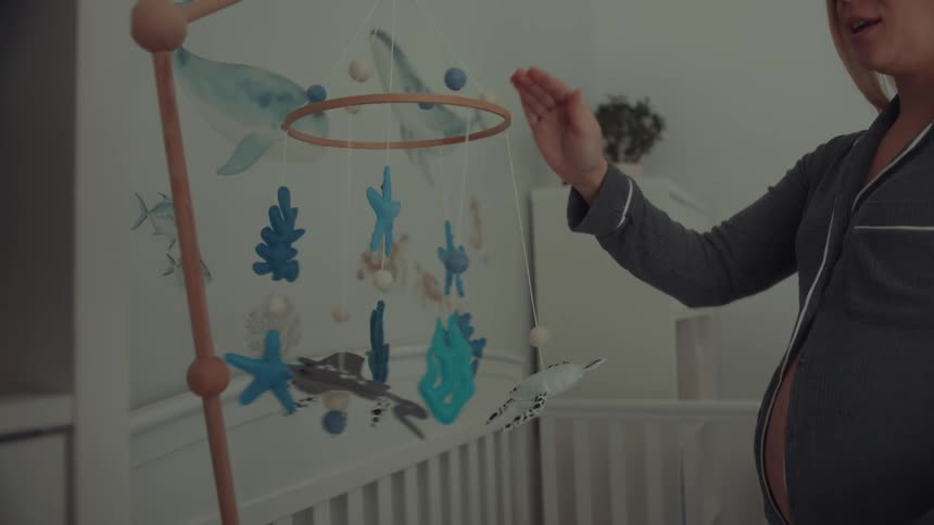 Expectant mother hangs a mobile above the crib