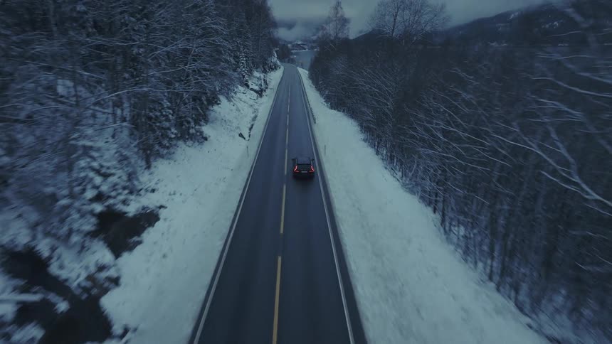 An aerial view of a car driving through a forest covered in snow