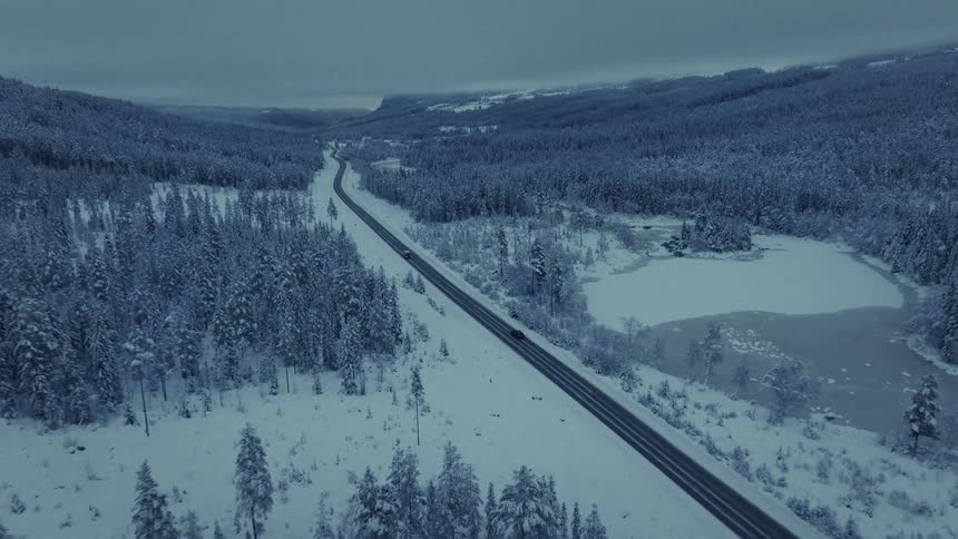 Van passes a truck traveling on a road through a snow covered forested mountain river valley