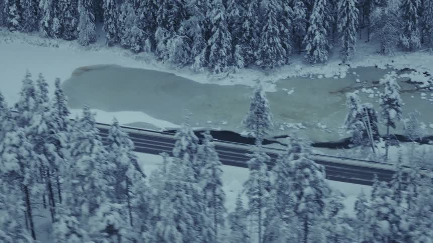 Van traveling on a forested mountain road along the coast overlooking a frozen river valley