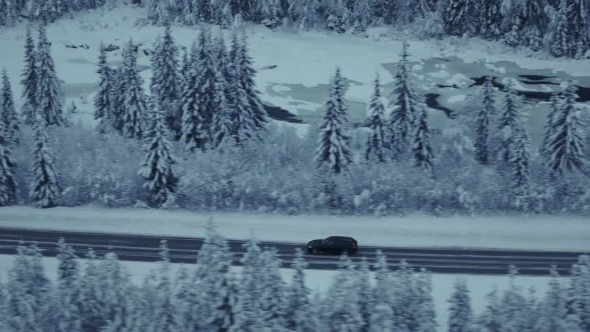 Van traveling on a forested mountain road along the coast overlooking a frozen river valley
