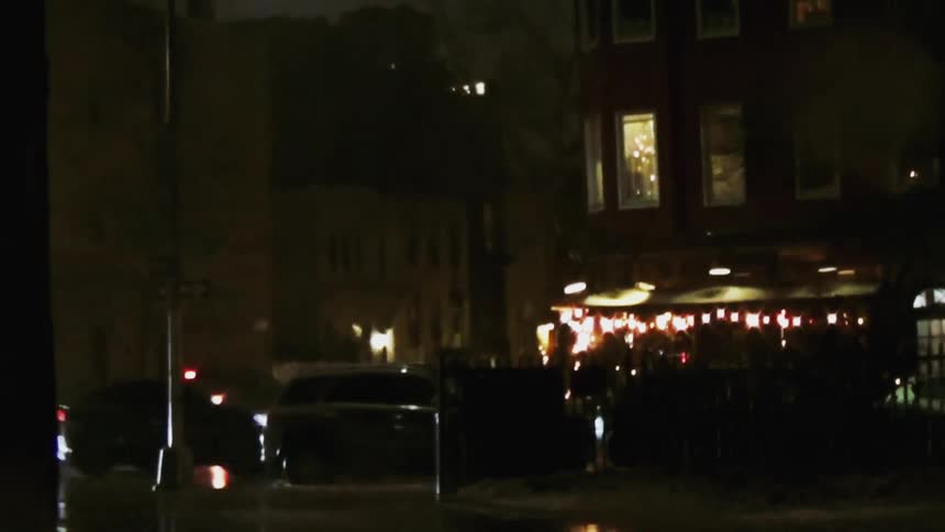 A street at night with cars driving by illuminated by streetlights with wet pavement from recent rain