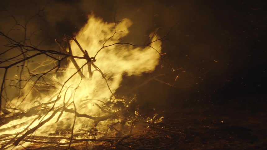 Brush burning in a field at night creates smoke and sparks