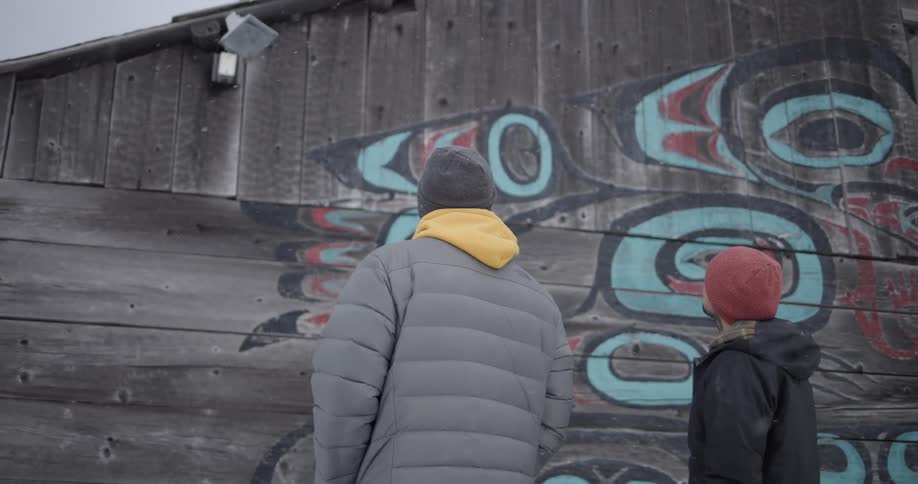 Two people observe a mural with colorful graphics on a wooden wall
