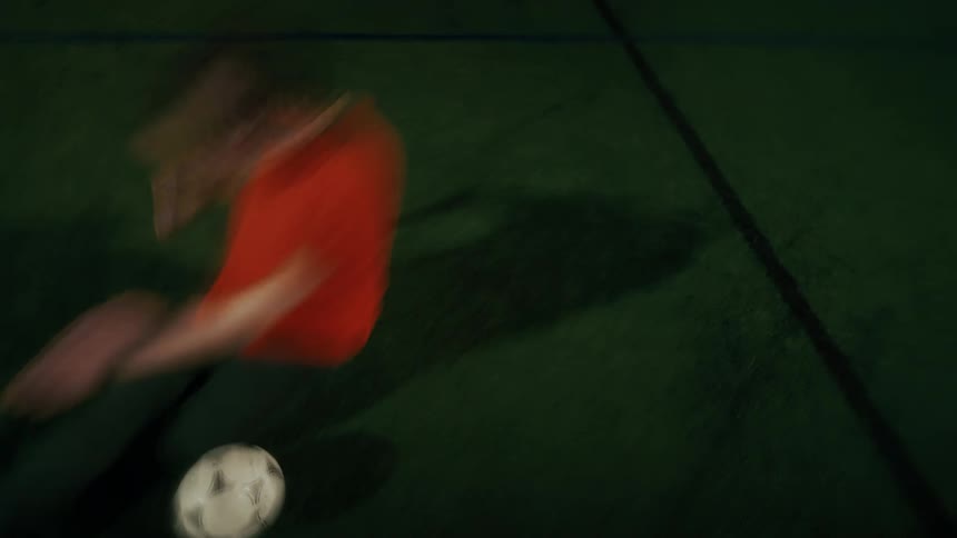 A firstperson perspective of someone playing soccer on an indoor turf field at night the camera follows the ball closely as the player dribbles across the green surface under bright stadium lighting