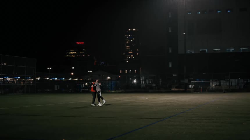 Two men talk on a lit soccer field at night