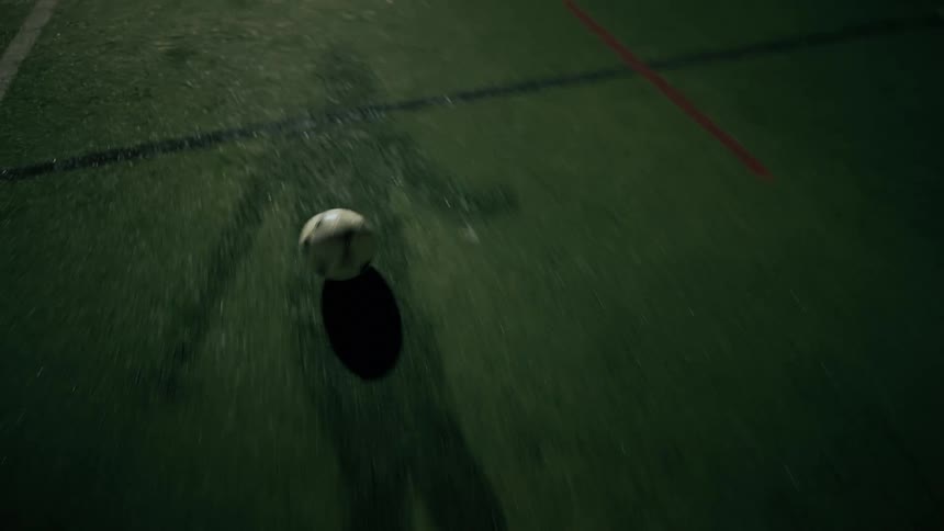 Player dribbling and kicking a soccer ball on a grass field at night