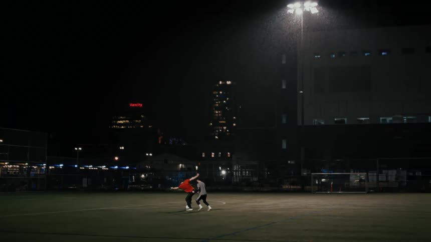 Two people playing soccer on a grass field at night in the rain