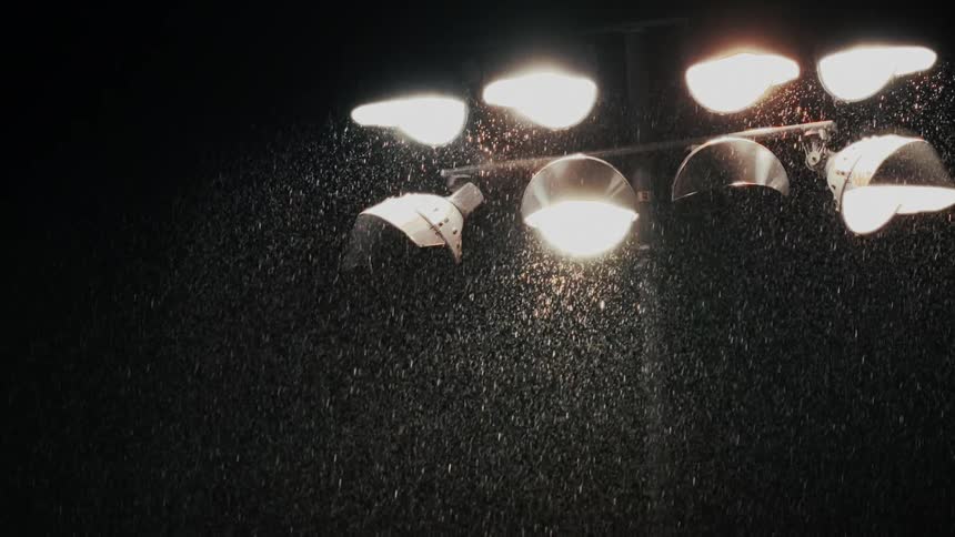 Rain falls at night time as an array of bright lights provide illumination