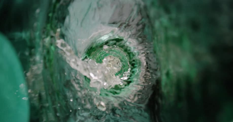 A view looking down into a green glass bottle shows clear liquid swirling into a whirlpool as it pours out