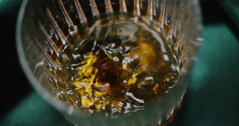 A topdown view shows ambercolored liquid swirling inside a textured glass creating ripples and reflections