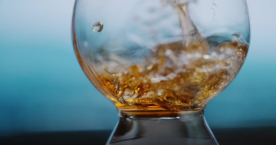 A stream of golden bourbon pours into a clear glass snifter where the liquid splashes and swirls against the sides