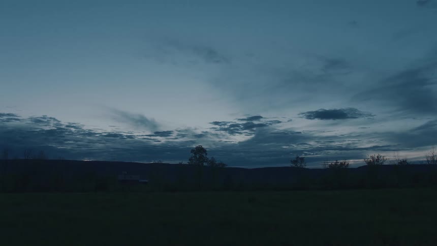 A vast rural field at twilight under a deep blue sky filled with thick grey clouds