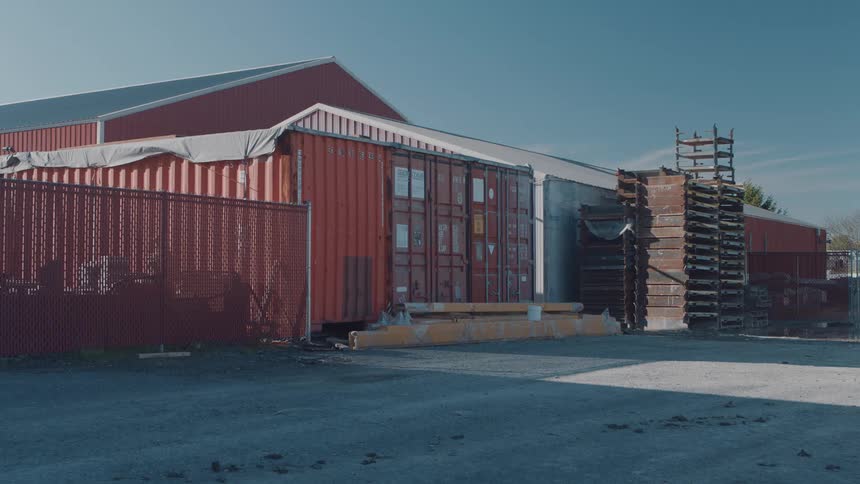 Containers and stacked pallets beside an industrial warehouse