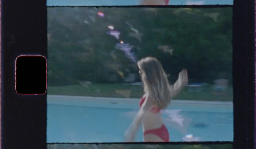 A young woman wearing a red bikini dances beside a swimming pool while colorful flags hang in the background