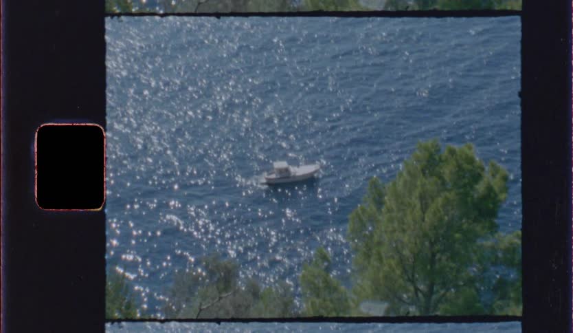 A boat docked near the shore of a lake with trees in the foreground along the shoreline at midday