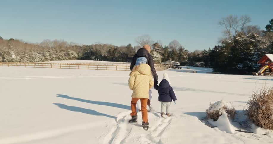 Woman walks through the snow in a rural field with her children