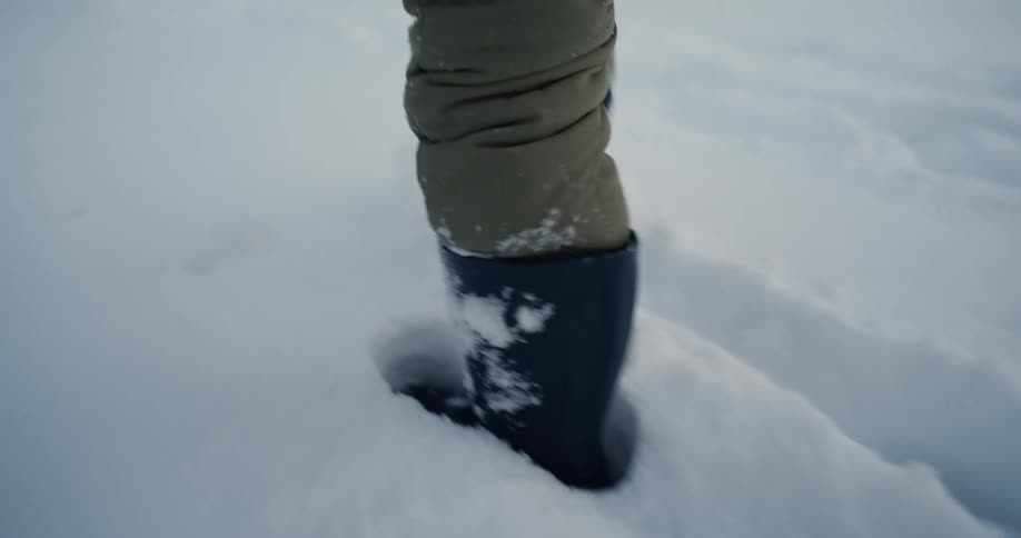 Black boots walking through deep snow with green padded pants