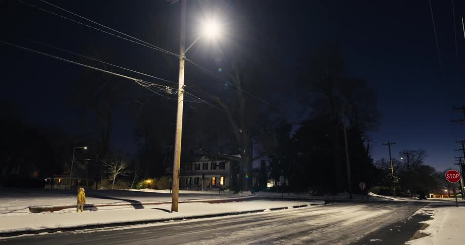 Snowcovered street with a lit streetlight at night and a child in the background