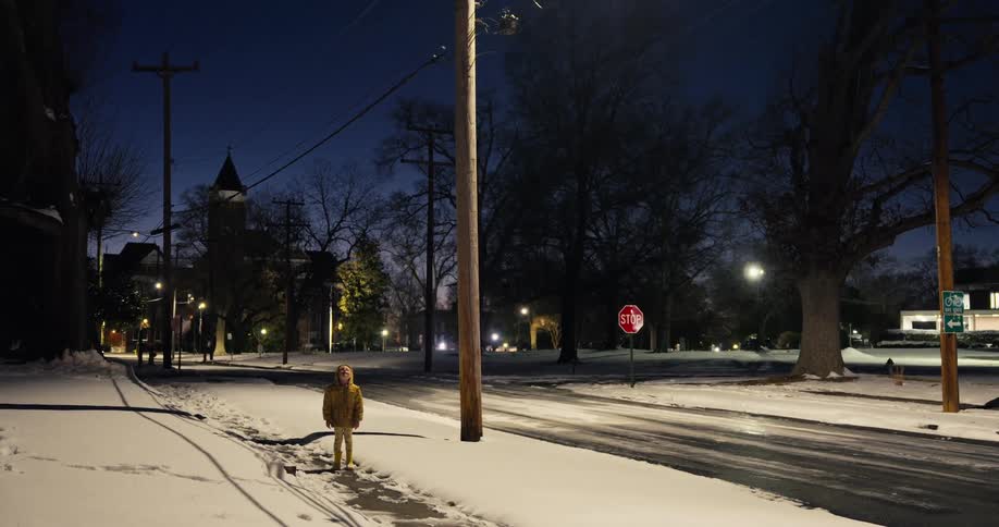A child standing outdoors in the snow at night