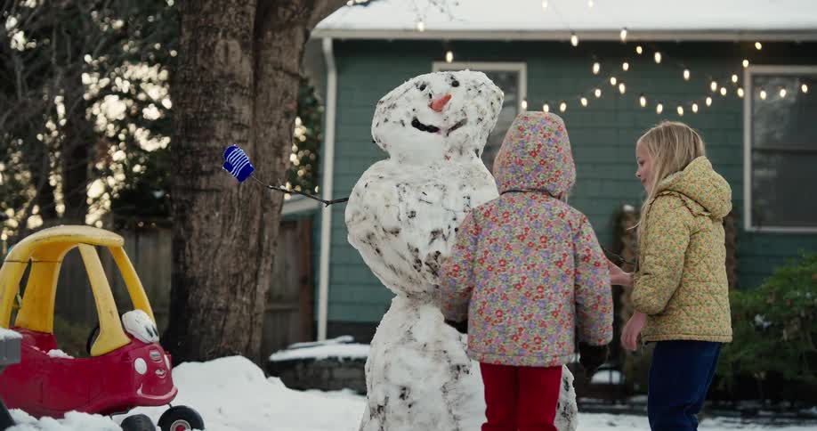 A mother and two children outdoors making a snowman