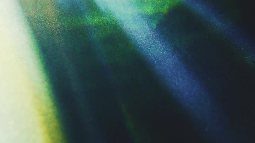 Streaks of vibrant blue and green light sweep across a dark textured surface creating a rhythmic dance of abstract flares and soft glimmers that flicker and fade in a continuous atmospheric and ethereal sequence