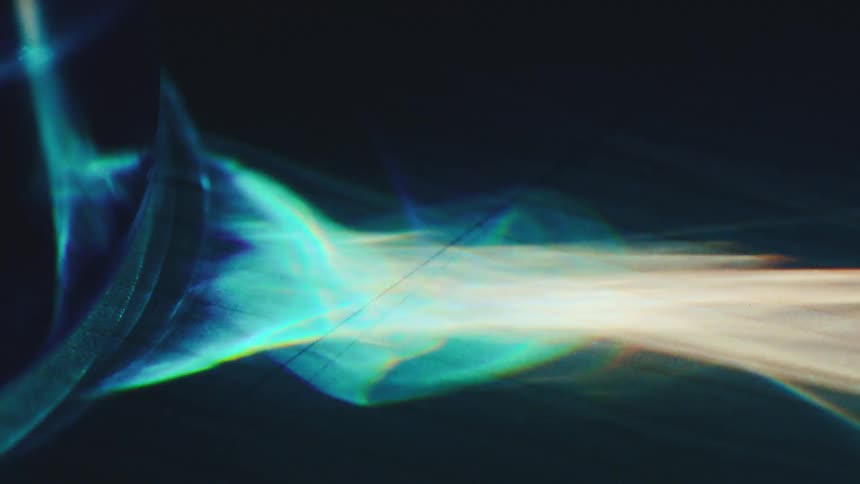 A close view of a glass object shows bright light refracting into colorful beams and patterns across a dark textured surface
