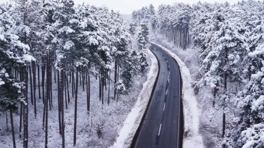 Winding road crossing a snowcovered forest seen from above