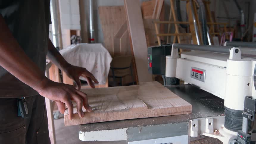 Man placing wood slab into planer machine in workshop