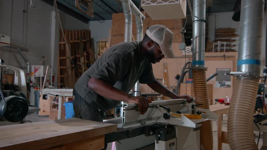 A man operates a jointer machine inside a professional woodworking shop