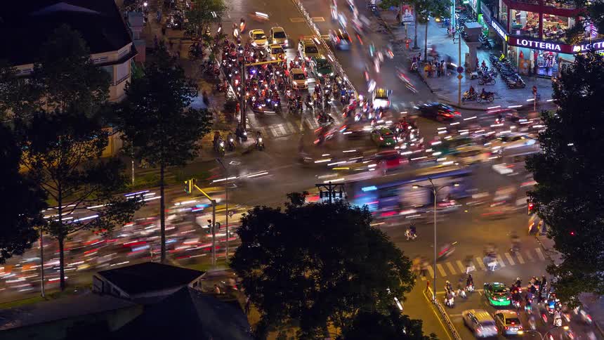 This timelapse video captures the highenergy flow of traffic at a busy urban intersection during the night the continuous motion of cars and motorbikes creates vibrant light trails that illuminate the streets and surrounding buildings