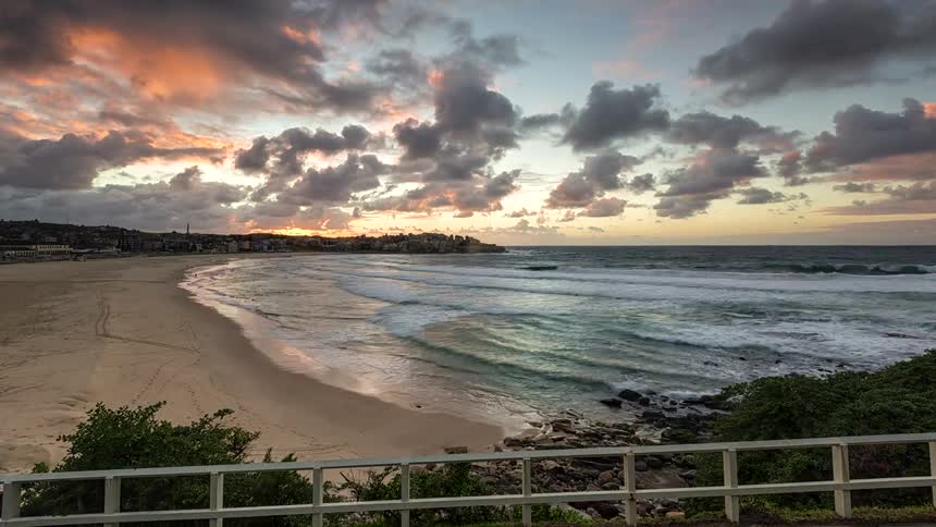 Sun rises over beach with waves and partly cloudy sky