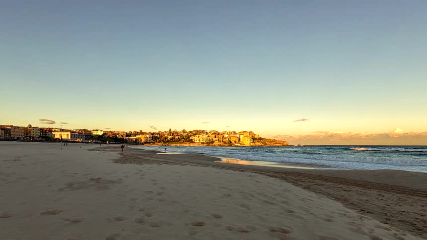 Beach with breaking waves and people walking under clear sky at sunset