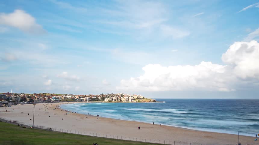 Town on the coast with buildings close together as people walk on the beach and waves roll in to shore