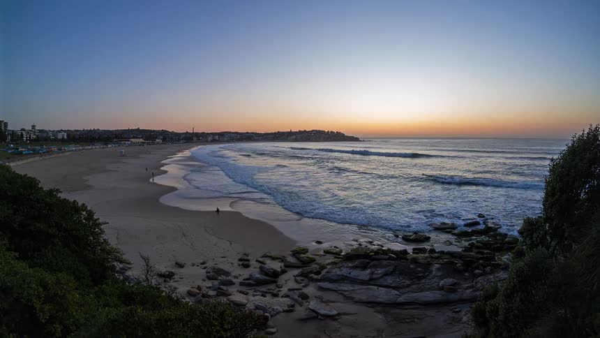 Sun rises on the horizon illuminating beach with waves and rock formations