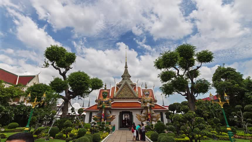 Temple with ornate facade guardian statues and symmetrical garden under partly cloudy sky
