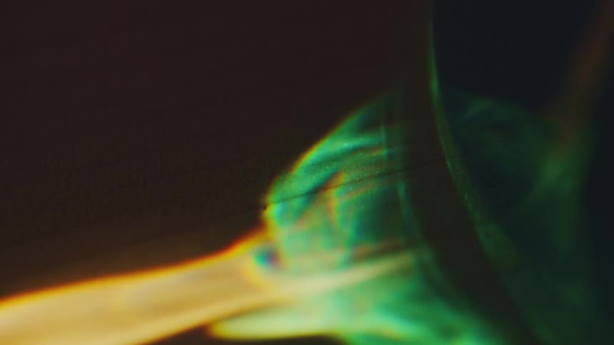 A beam of light passing through glass to create a vivid rainbow refraction that moves across a dark textured surface