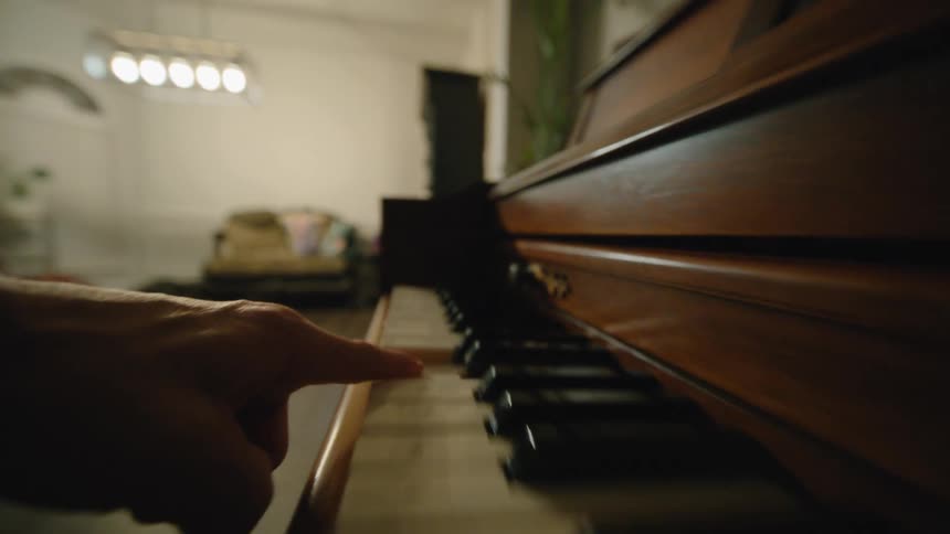 A persons hand plays a grand piano indoors striking the keys from left to right and then from right to left