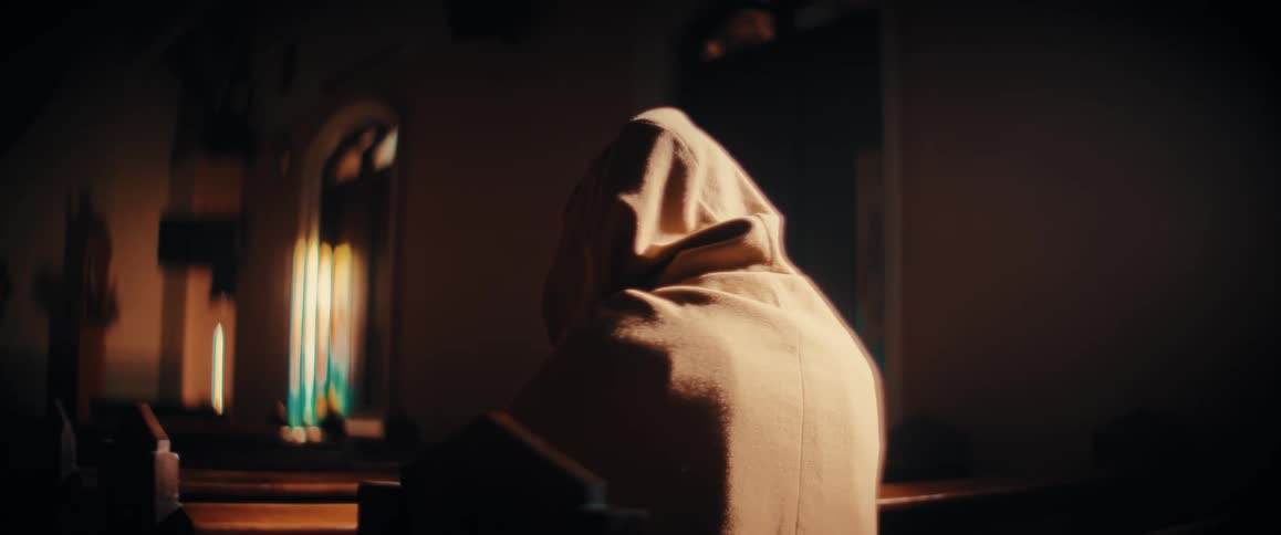 A person in hooded robe sitting in church pew