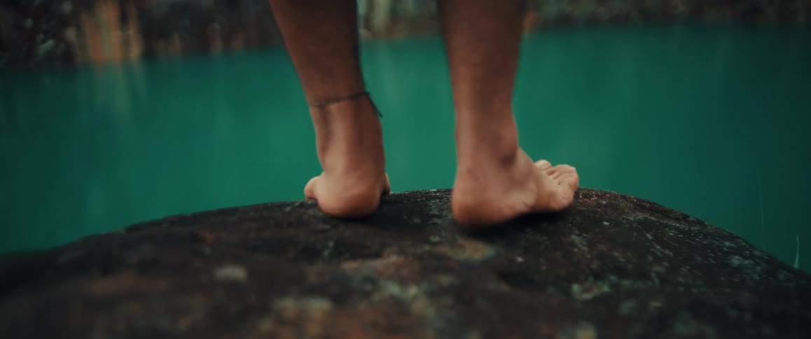 Bare feet resting on a rock at the edge of turquoise water