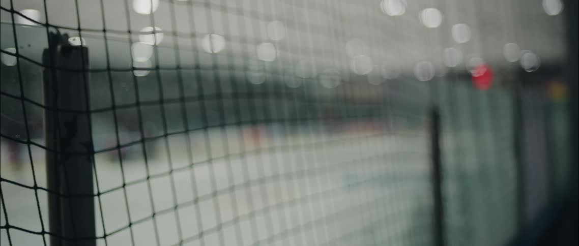A dark thin safety net creates a grid of intersecting horizontal and vertical lines that remain in sharp focus in the foregroundbehind the netting the blurred background shows the long horizontal white and blue lines of an ice hockey rink