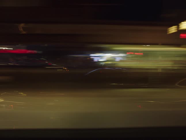 The cars drive by the brightly lit buildings at night