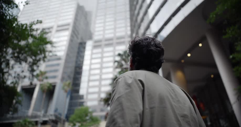 A man stands outside a skyscraper and looks up on a summer day