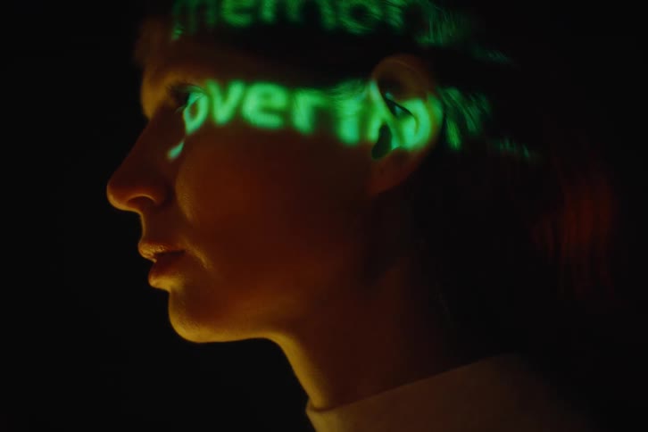 Green words are projected onto the face of a person standing and staring in the dark