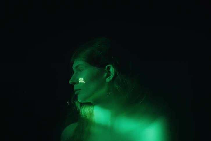 A womans profile is seen in darkness with green light and flickering lines of text projected onto her face