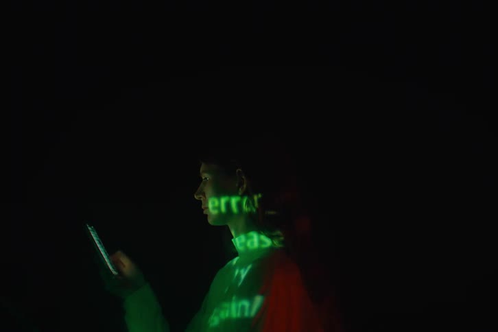 The woman is texting on her cell phone in the dark room