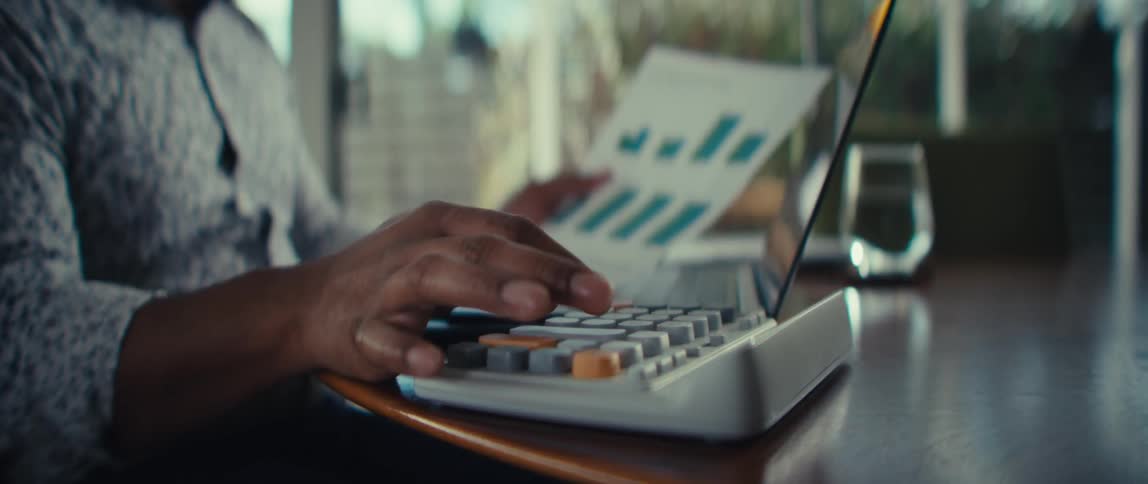 A man seated at a table uses a calculator while holding a document
