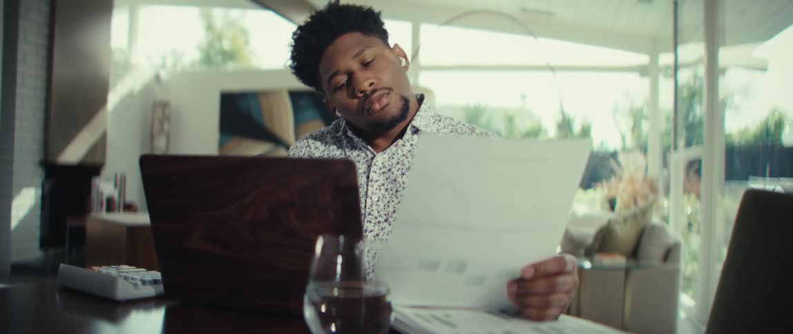 The man is reading a paper and using his laptop
