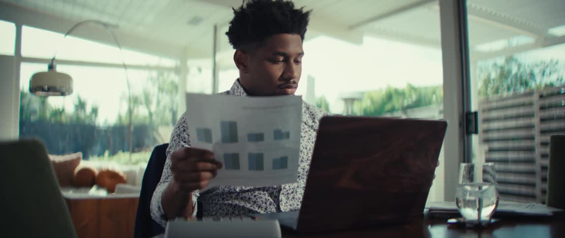 A man sits at a table looking at papers and a laptop