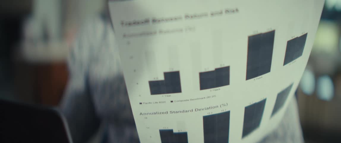 A focused black man in a patterned shirt looks down while holding a financial document